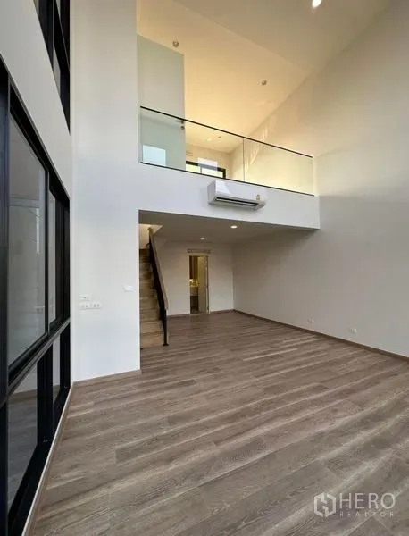 Townhouse for rent in Yan Nawa, Bangkok - Spacious double-height living area with mezzanine level and wood floors.