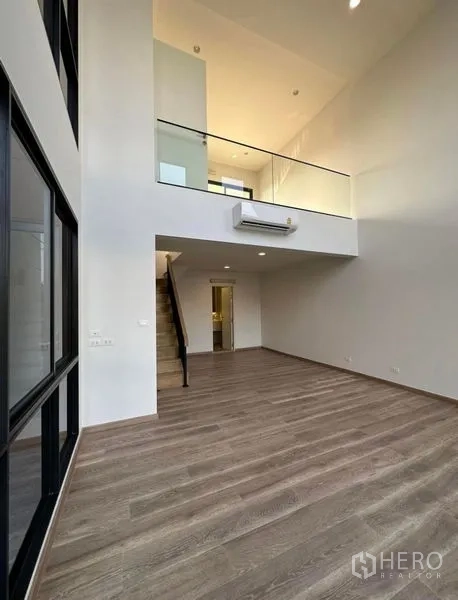 Townhouse for rent in Yan Nawa, Bangkok - Spacious double-height living area with mezzanine level and wood floors.