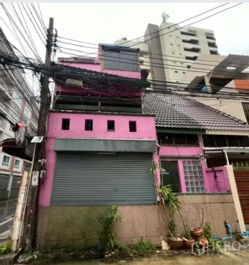 อาคารพาณิชย์ ให้เช่าในWatthana, Bangkok - มุมมองด้านหน้าอาคารพาณิชย์สีชมพูหลายชั้น พร้อมประตูม้วนและหลังคากระเบื้อง ในเขตวัฒนา กรุงเทพฯ