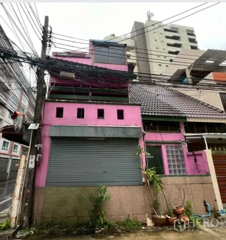 อาคารพาณิชย์ ให้เช่าในWatthana, Bangkok - มุมมองด้านหน้าอาคารพาณิชย์สีชมพูหลายชั้น พร้อมประตูม้วนและหลังคากระเบื้อง ในเขตวัฒนา กรุงเทพฯ