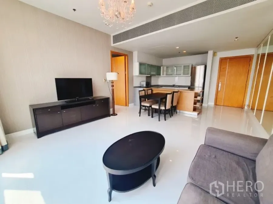 Condominium for rent in Khlong Toei, Bangkok - Living area with sofa, chandelier, TV console and dining set beside the kitchen.