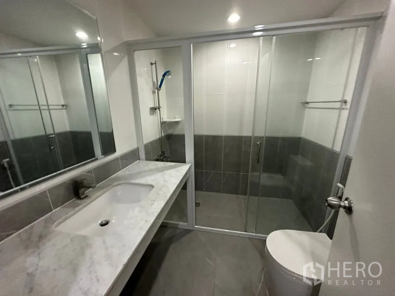 公寓 出租在Watthana, Bangkok - 现代卫浴设长条大理石洗手台、坐便器与玻璃淋浴房。