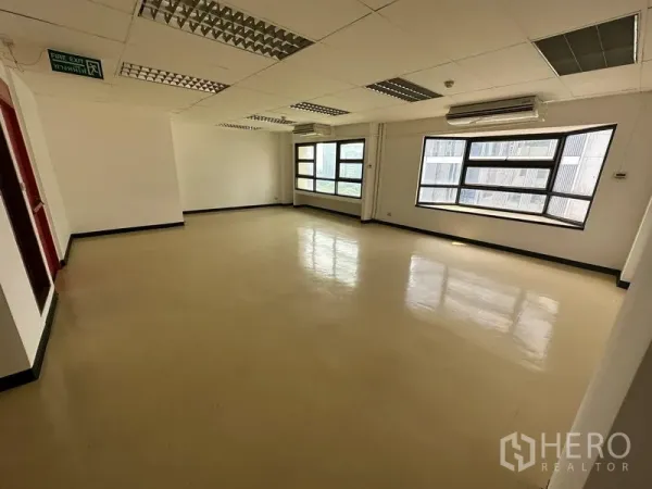 Office Space for rent in Pathum Wan, Bangkok - Corner office zone with wraparound windows, wall-mounted AC units and an emergency exit sign.