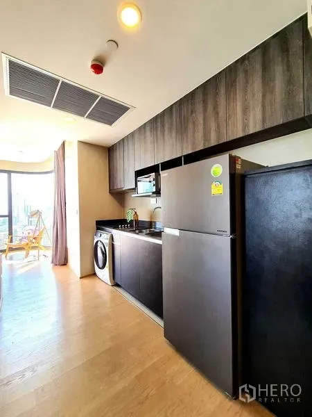Condominium for rent in Bang Rak, Bangkok - Modern galley kitchen with dark wood cabinets, refrigerator, microwave, sink and washing machine.