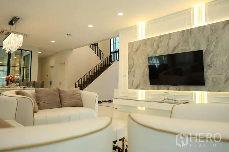 Detached House for rent or sale in Saphan Sung, Bangkok - Living room with circular sofas, marble TV feature and staircase view.