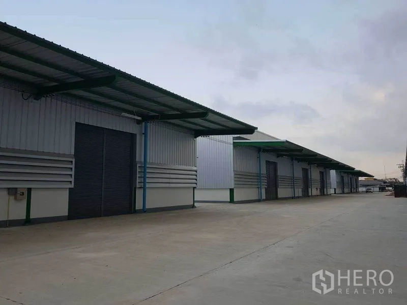 Warehouse for rent in Prawet, Bangkok - Multiple warehouse units with canopies and roller shutters facing a large maneuvering area.
