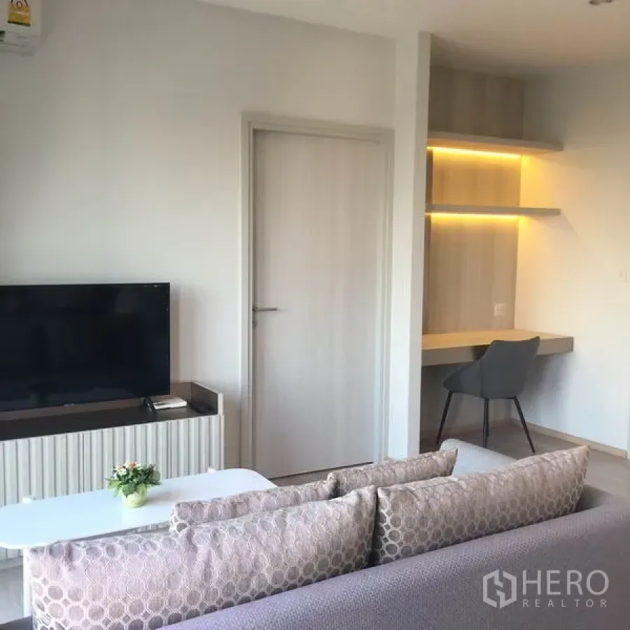 Condominium for rent in Huai Khwang, Bangkok - Bright living room with TV console, sofa and a built‑in illuminated work desk.