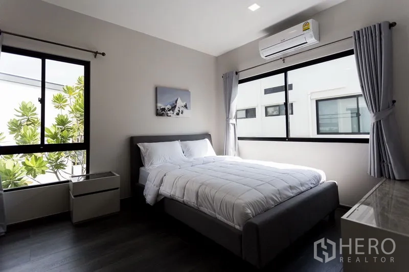 Townhouse for rent in Samut Prakan - Sunlit secondary bedroom with double bed, big windows and AC overlooking greenery.