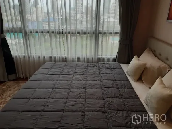 公寓 出租在Watthana, Bangkok - 主卧配大窗城市景观，灰色被褥的双人床与米色靠枕。