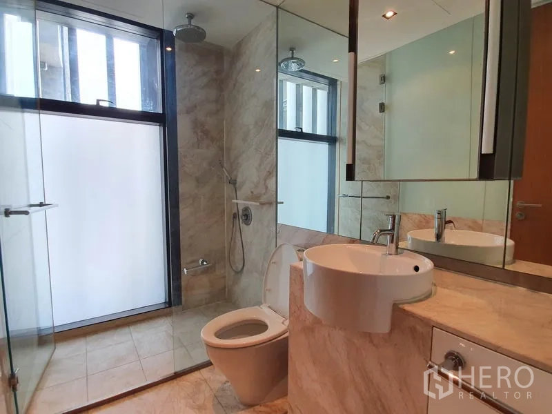 Condominium for rent in Sathon, Bangkok - Second bathroom with marble walls, large mirror and glass shower enclosure.