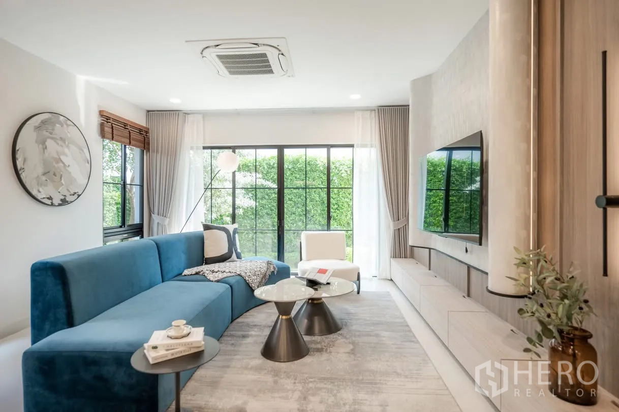 Detached House for rent in Saphan Sung, Bangkok - Living room with blue sectional sofa, large windows, and glass doors facing greenery.