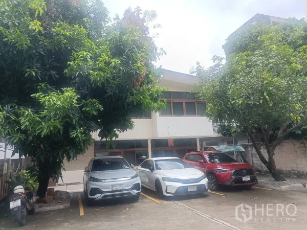 独立式住宅 出租在Bang Rak, Bangkok - 前院停车区，三辆车停在树荫下，对面是房子。