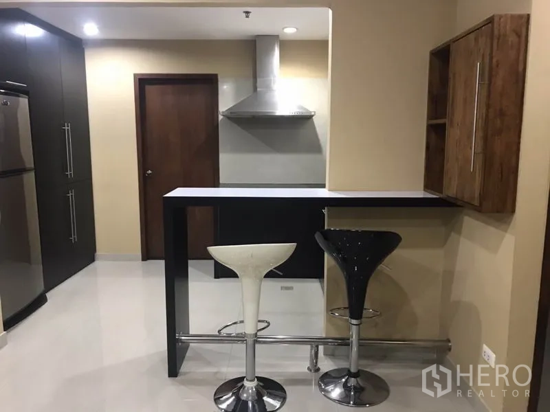 Condominium for rent in Watthana, Bangkok - Kitchen breakfast bar with two stools, stainless range hood and fridge.