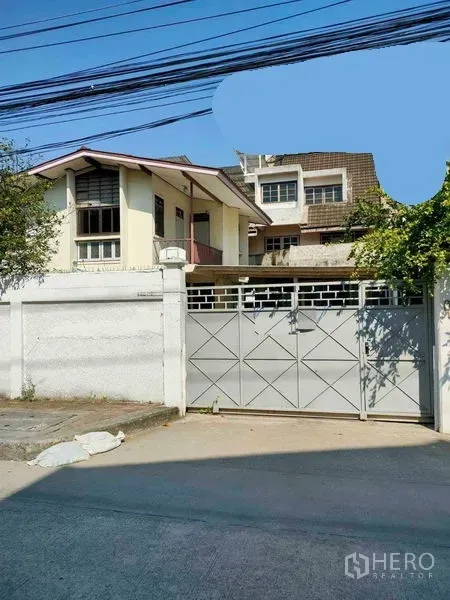 Retail Space for rent in Yan Nawa, Bangkok - Street-facing compound with a high white wall and sliding metal gate, two-storey gabled building inside and trees along a concrete road.