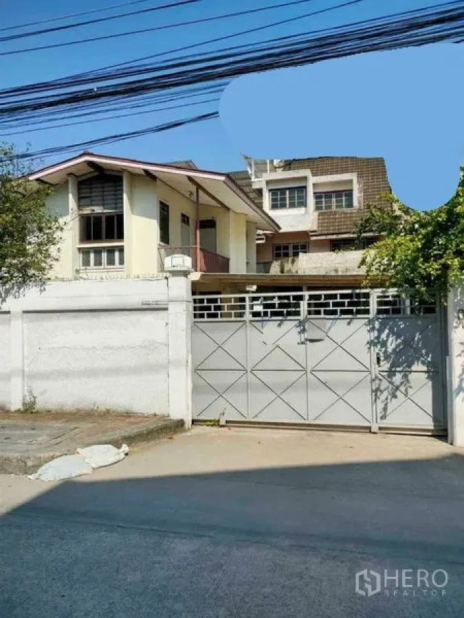 Retail Space for rent in Yan Nawa, Bangkok - Street-facing compound with a high white wall and sliding metal gate, two-storey gabled building inside and trees along a concrete road.