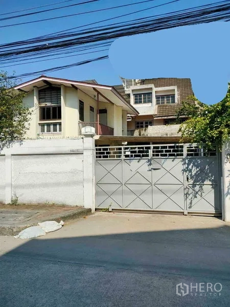 Retail Space for rent in Yan Nawa, Bangkok - Street-facing compound with a high white wall and sliding metal gate, two-storey gabled building inside and trees along a concrete road.