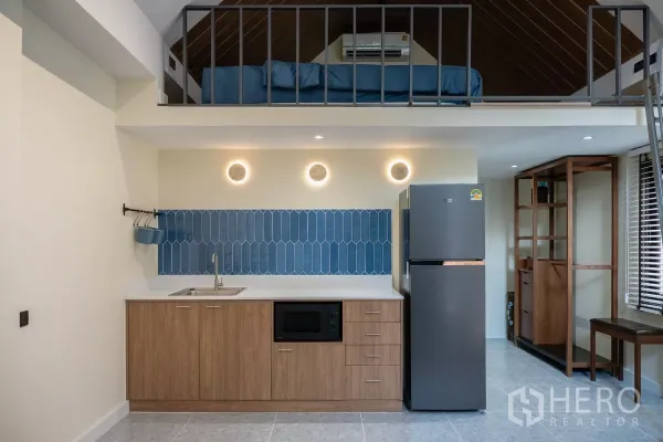 Detached House for rent in Phra Khanong, Bangkok - Compact kitchen with wood cabinets, blue tile backsplash, refrigerator and a loft sleeping area above.