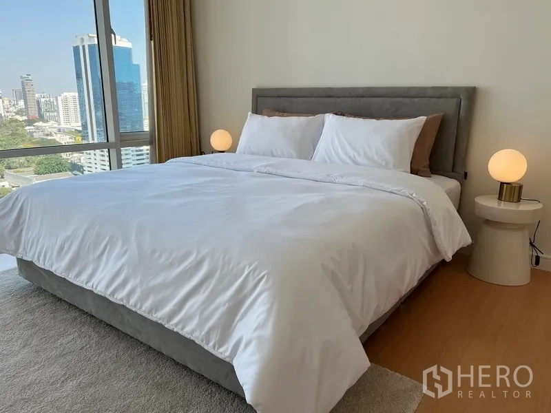 公寓 出租在Watthana, Bangkok - 主卧配特大床与床头灯，窗外为全景城市景观。