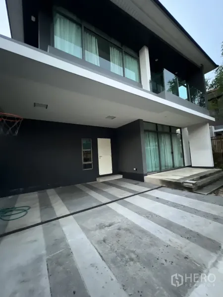 Detached House for rent or sale in Bang Kapi, Bangkok - Covered carport and striped concrete driveway beneath the balcony.