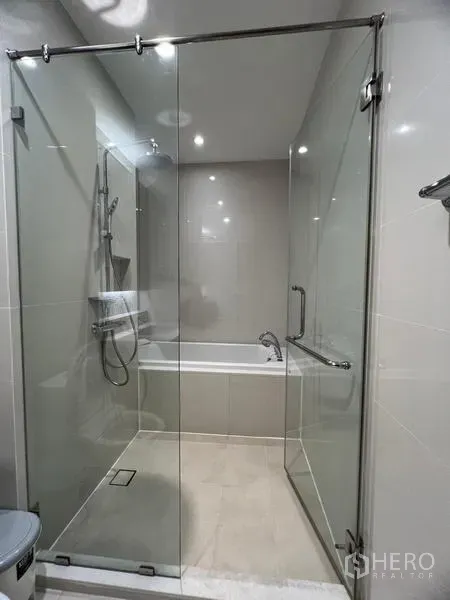 Condominium for rent in Khlong Toei, Bangkok - Contemporary bathroom featuring a glass-enclosed rain shower with a separate bathtub behind.