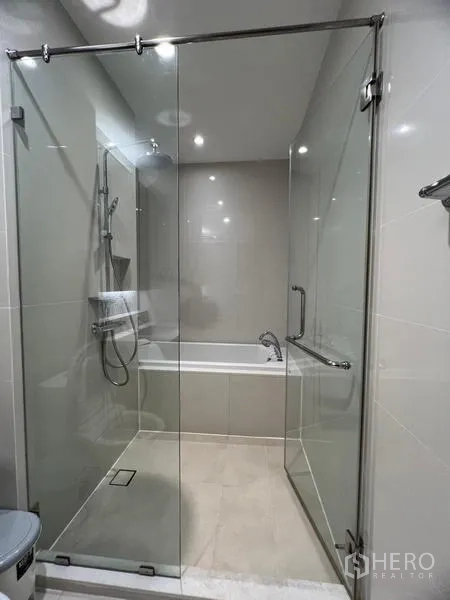 Condominium for rent in Khlong Toei, Bangkok - Contemporary bathroom featuring a glass-enclosed rain shower with a separate bathtub behind.