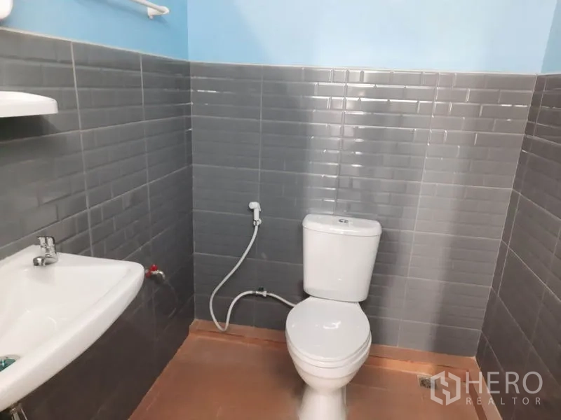 Warehouse for rent in Khlong Luang, Pathum Thani - Clean tiled restroom inside the warehouse with sink, toilet and handheld bidet spray.