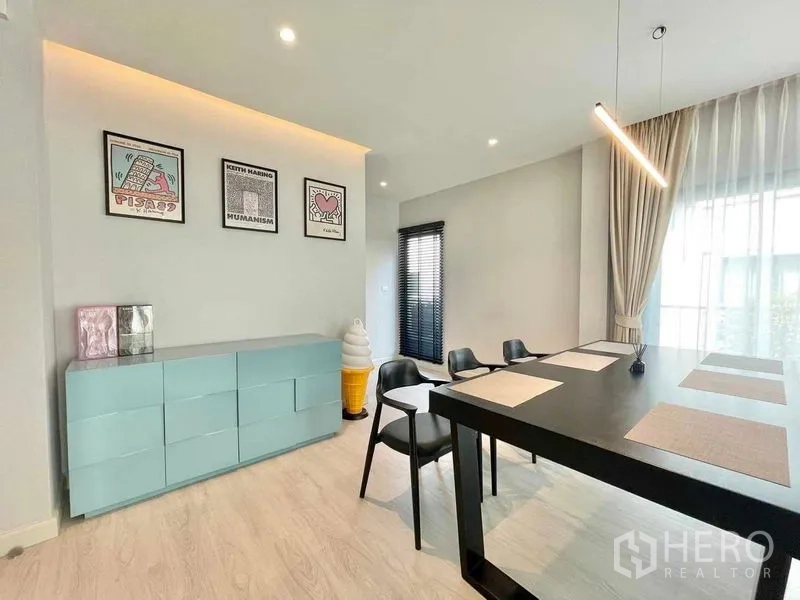 บ้าน ให้เช่าในBang Phli, Samut Prakan - มุมทานอาหาร โต๊ะสีดำ โคมไฟแขวน และตู้บัฟเฟต์สีพาสเทลพร้อมกรอบภาพ