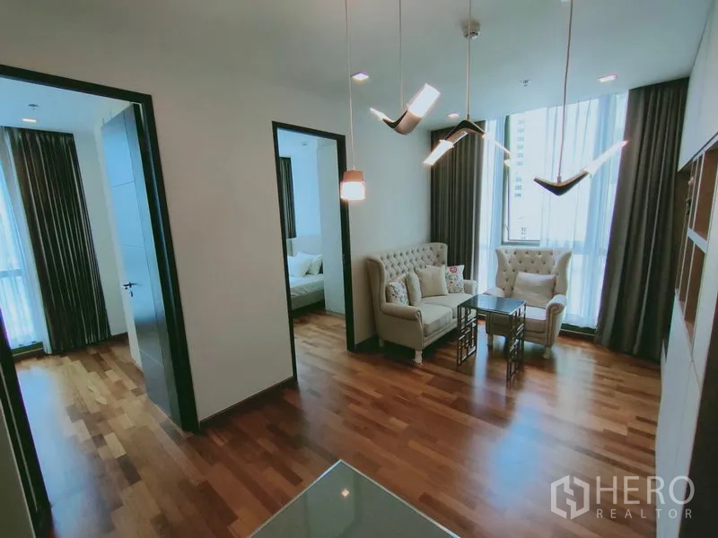 公寓 出租在Ratchathewi, Bangkok - 从客厅望向两间卧室，设计感吊灯与木地板相映成趣。