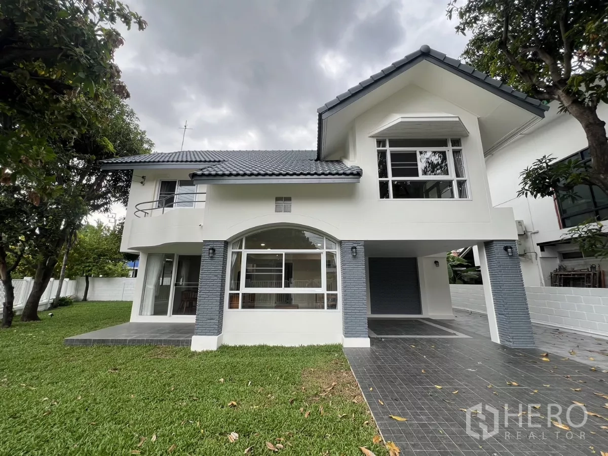 Detached House for rent in Saphan Sung, Bangkok - Two-storey white detached house with tiled roof, large front lawn and mature trees.