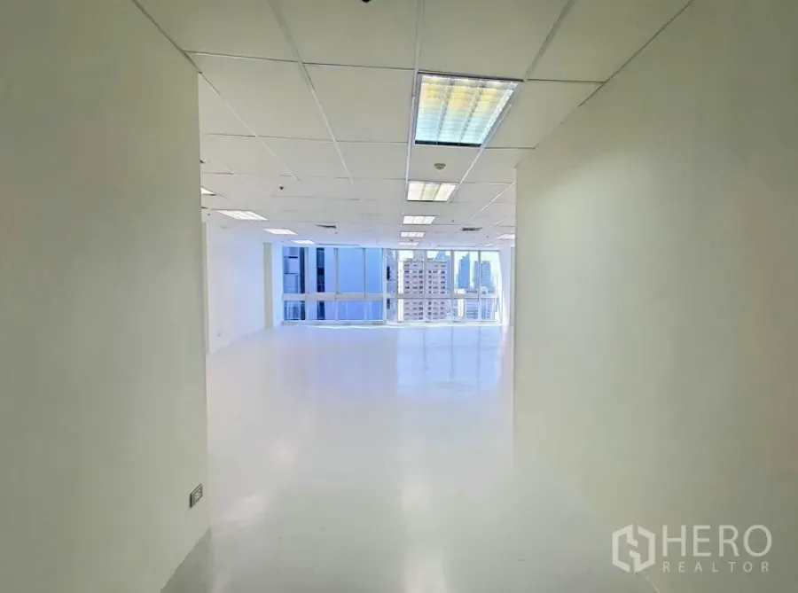 Office Space for rent in Khlong Toei, Bangkok - Bright entry corridor opening to an open‑plan office with white floors, drop‑ceiling lights, and large windows showing Bangkok skyline views.