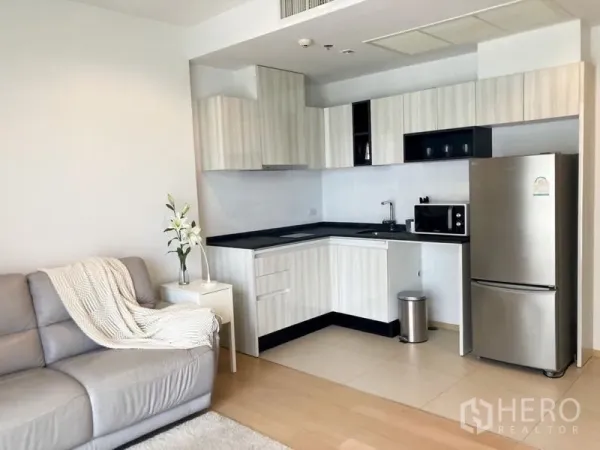 公寓 出租在Watthana, Bangkok - 明亮客厅与L形开放式厨房，配不锈钢冰箱和沙发的曼谷公寓