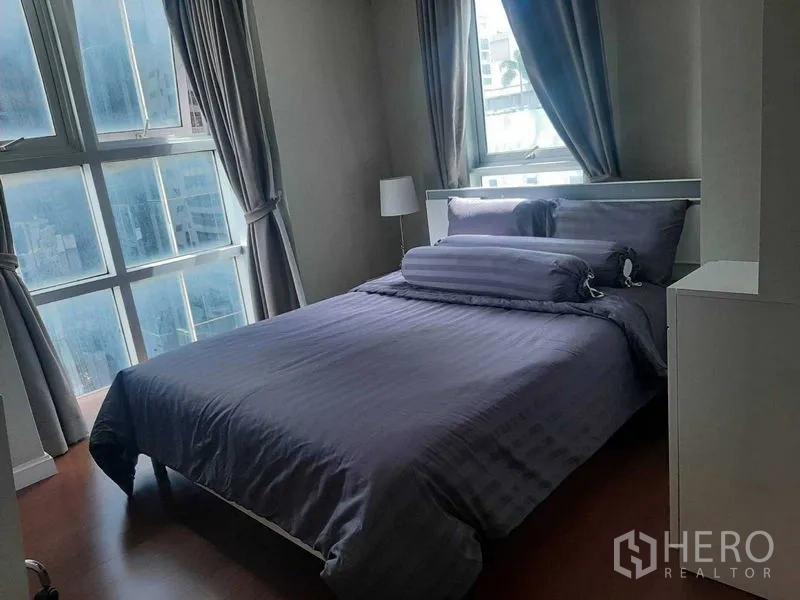 คอนโด ให้เช่าหรือขายในHuai Khwang, Bangkok - ห้องนอนมุมอาคาร หน้าต่างบานใหญ่หลายช่อง ผ้าม่านสีเทา และวิวเมือง