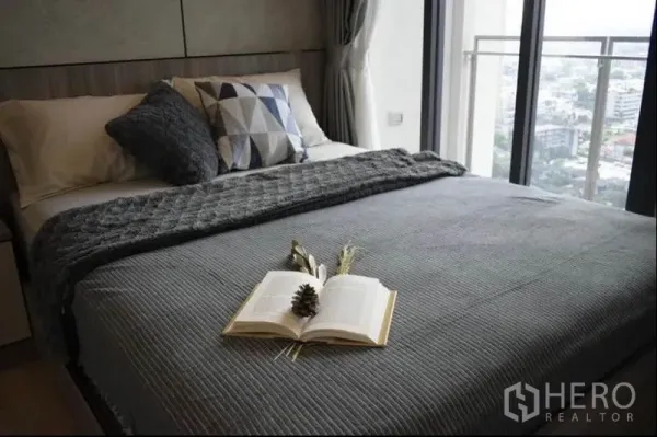 Condominium for rent or sale in Phaya Thai, Bangkok - Bedroom with grey bedding and balcony doors opening to a city skyline view.