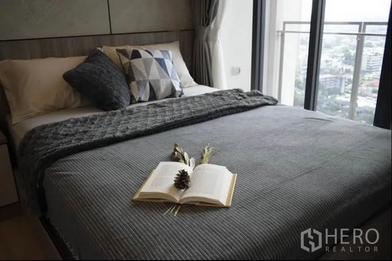 Condominium for rent or sale in Phaya Thai, Bangkok - Bedroom with grey bedding and balcony doors opening to a city skyline view.