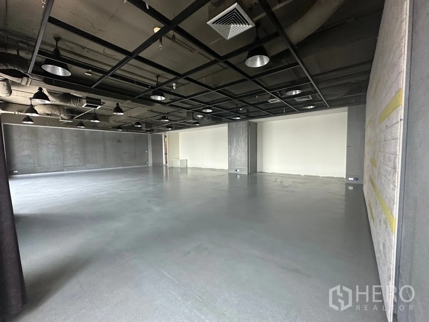 Office Space for rent in Khlong Toei, Bangkok - Industrial-style open room with grid lighting and exposed concrete walls.