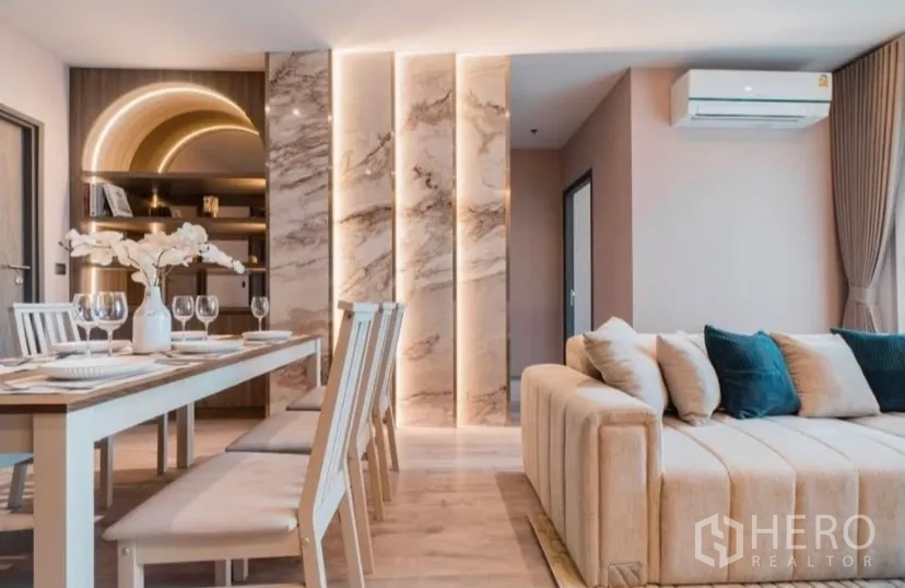 Condominium for rent in Watthana, Bangkok - Living–dining space with tufted sofa and vertical marble light columns.