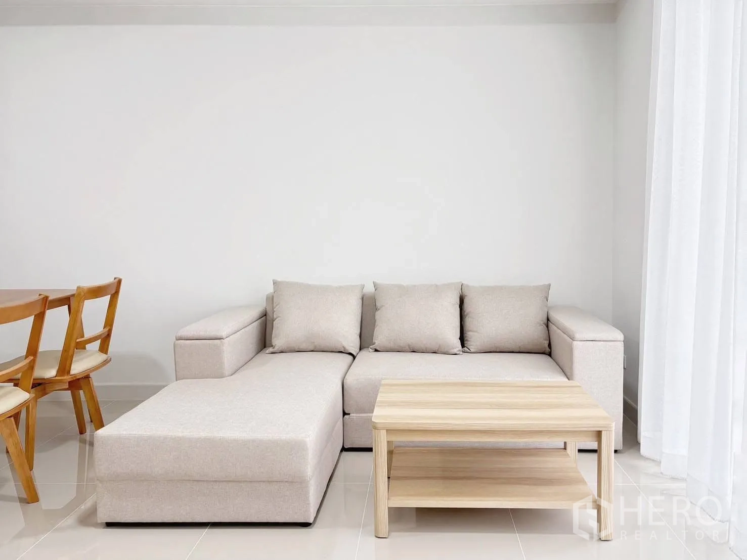 Townhouse for rent in Bang Phli, Samut Prakan - Neutral-toned lounge with sectional sofa and wooden coffee table beside sheer curtains.