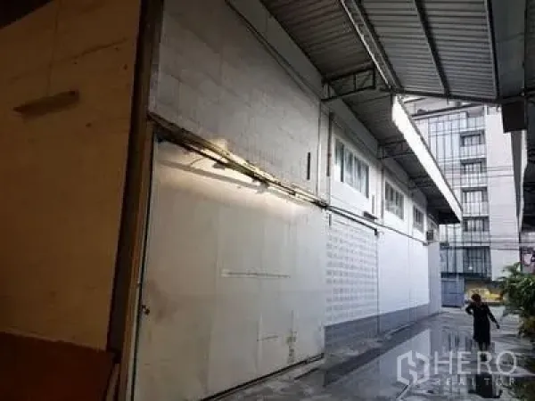 คลังสินค้า ให้เช่าในChatuchak, Bangkok - ทางขนถ่ายสินค้ากึ่งในร่มริมกำแพงโกดังสีขาว หลังคาโลหะสูง มีรางระบายน้ำ และอาคารสมัยใหม่ใกล้เคียง ใกล้รัชดาภิเษก
