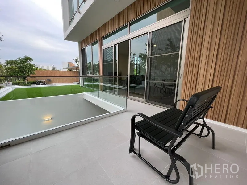 Detached House for rent or sale in Saphan Sung, Bangkok - Covered terrace with glass railing overlooking a private lawn and sliding glass doors.