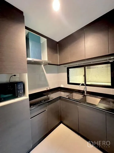 Townhouse for rent in Saphan Sung, Bangkok - Alternate view of the L-shaped kitchen showing sink, hob and glossy cabinetry.