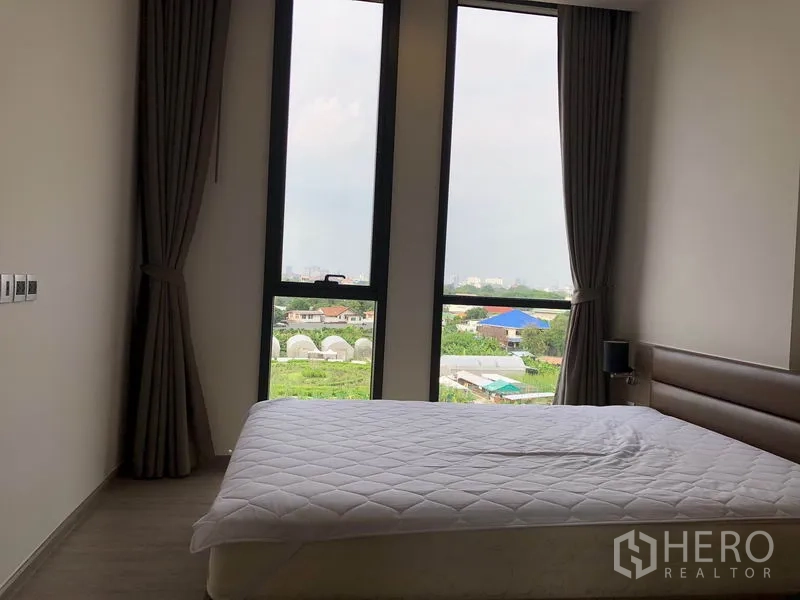 Condominium for rent in Watthana, Bangkok - Cozy bedroom with tall windows, curtains, and garden and skyline views from Mori Haus.