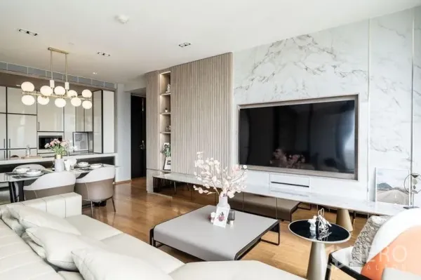 Condominium for rent in Khlong Toei, Bangkok - Bright living room with marble feature wall, large TV, and open-plan dining in a luxury Bangkok condo.