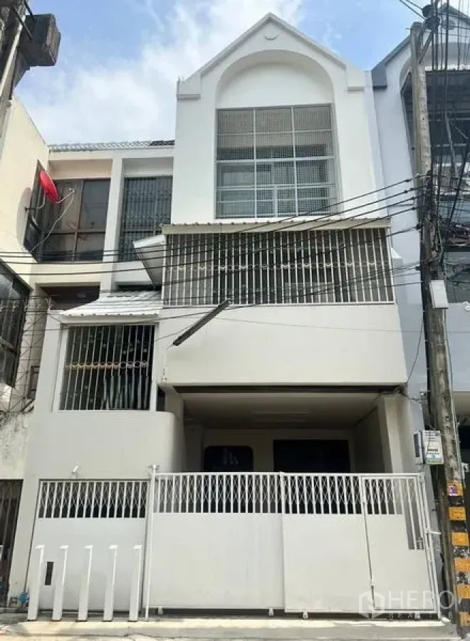 联排别墅 出售在Khlong Toei, Bangkok - 三层白色联排别墅外立面，带围栏车位、金属护栏窗和阳台，位于素坤逸一带，晴天拍摄。