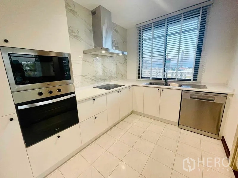 Condominium for rent - L-shaped white kitchen with oven, cooktop, and large window.
