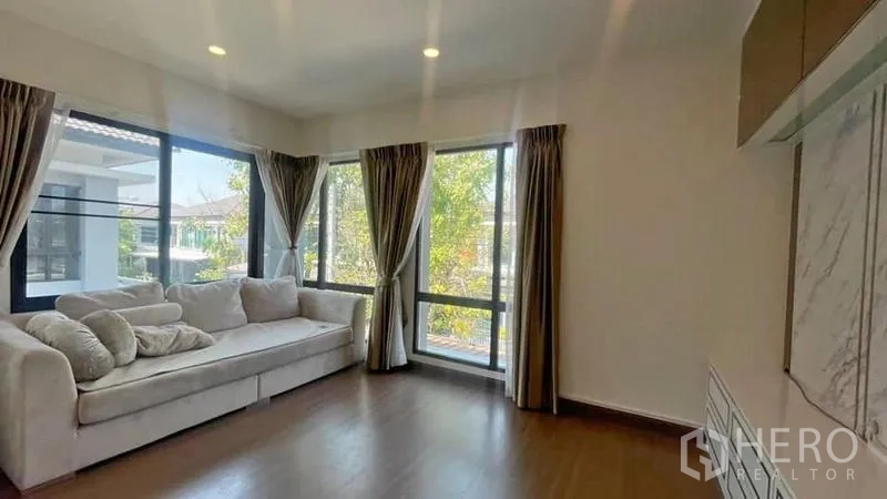 Detached House for rent or sale in Prawet, Bangkok - Corner family lounge with L-shaped sofa, floor-to-ceiling windows and garden views.