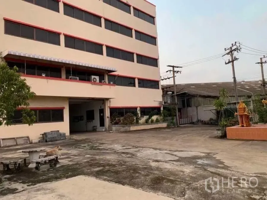 Factory for rent in Samut Prakan - Exterior of a multi-storey factory office building with a wide concrete yard and a covered loading entrance.