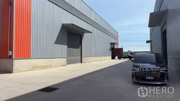 Warehouse for rent in Bang Bo, Samut Prakan - Modern metal-clad warehouse exterior with roller shutter loading bays and a wide driveway for trucks.