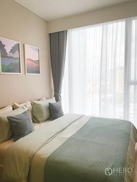 Condominium for sale in Khlong Toei, Bangkok - Sunlit bedroom with a queen bed, soft textiles, and floor-to-ceiling window with sheer curtains.