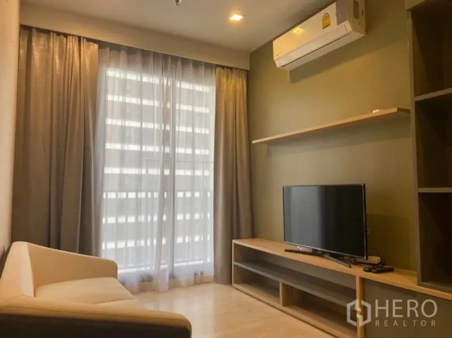 Condominium for rent in Watthana, Bangkok - Cozy living room with sofa, TV console, open shelving and floor-to-ceiling drapes.