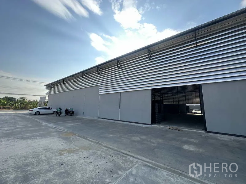 Warehouse for rent in Lam Luk Ka, Pathum Thani - Side exterior with vented cladding, sliding entry and large paved area for truck parking and maneuvering.